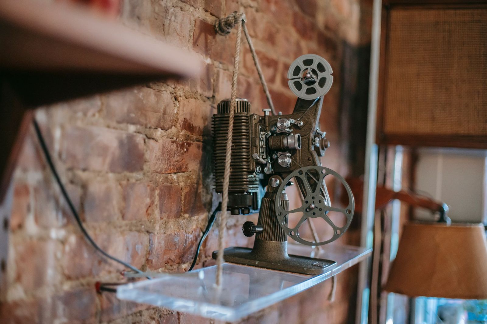 A vintage film projector on a shelf against a brick wall