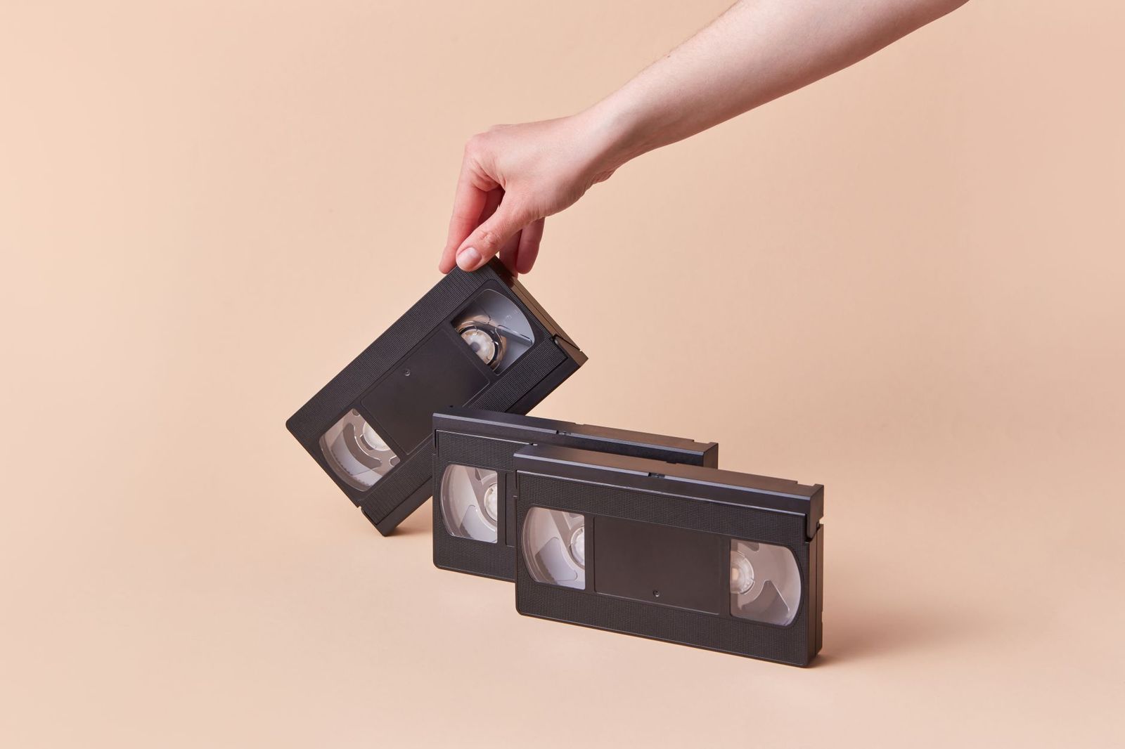 A hand holding a VHS tape against a parchment-colored wall