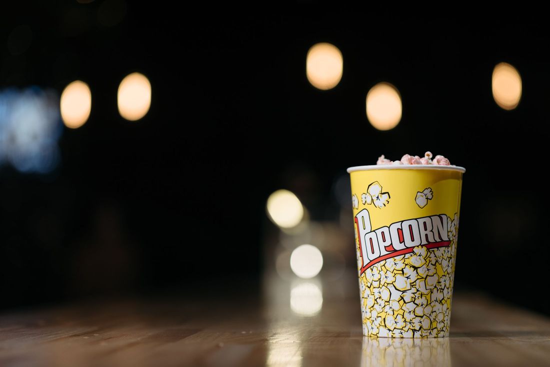 A cup of popcorn on a wooden counter with warm lights behind