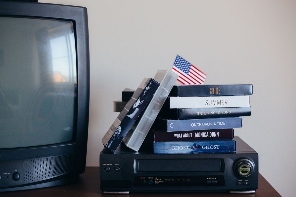 A stack of VHS tapes beside a vintage television and VCR