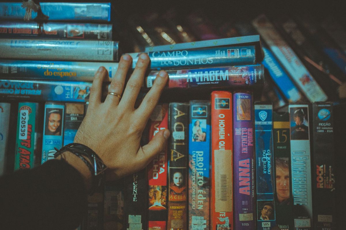 A hand pulling a VHS tape from a packed shelf